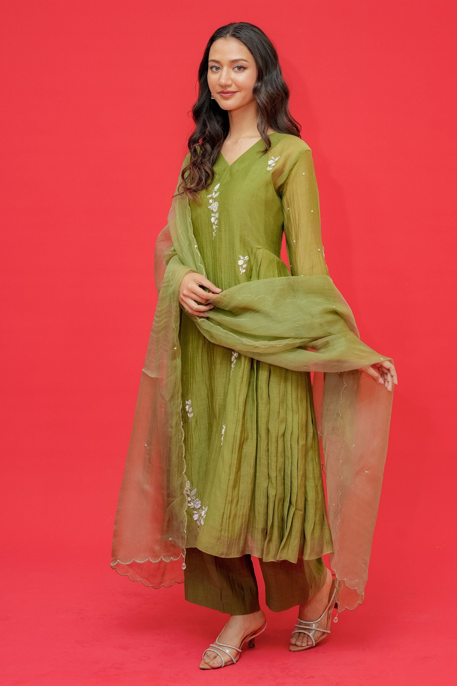 Woman in a green traditional outfit with a dupatta against a red background