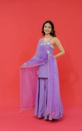 Woman in a purple traditional outfit with a sheer dupatta against a red background