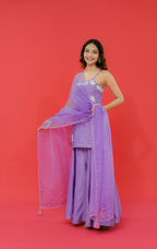 Woman in a purple traditional outfit with a sheer dupatta against a red background