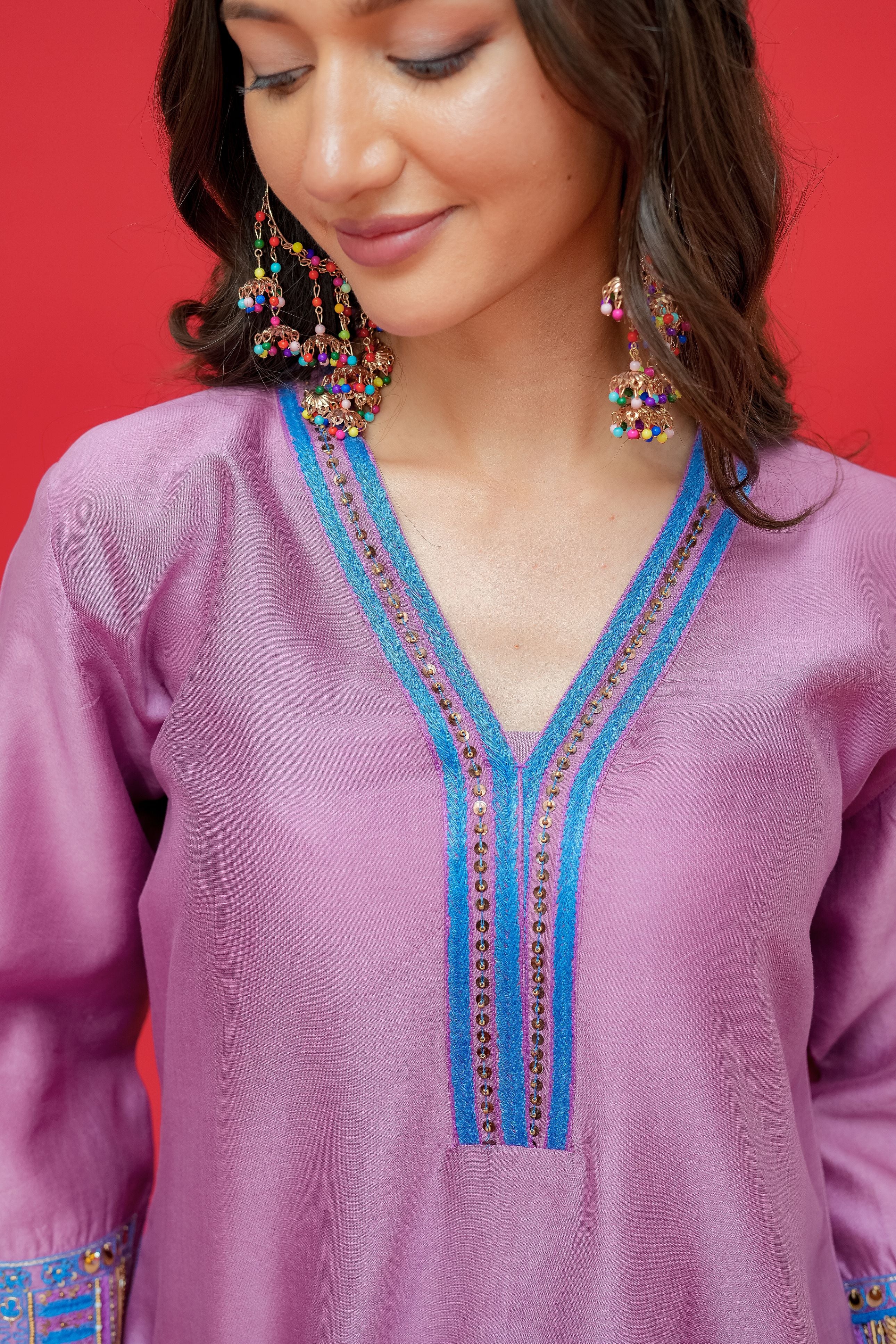 Woman wearing a purple embroidered top with blue accents against a red background