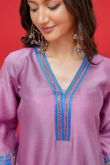 Woman wearing a purple embroidered top with blue accents against a red background