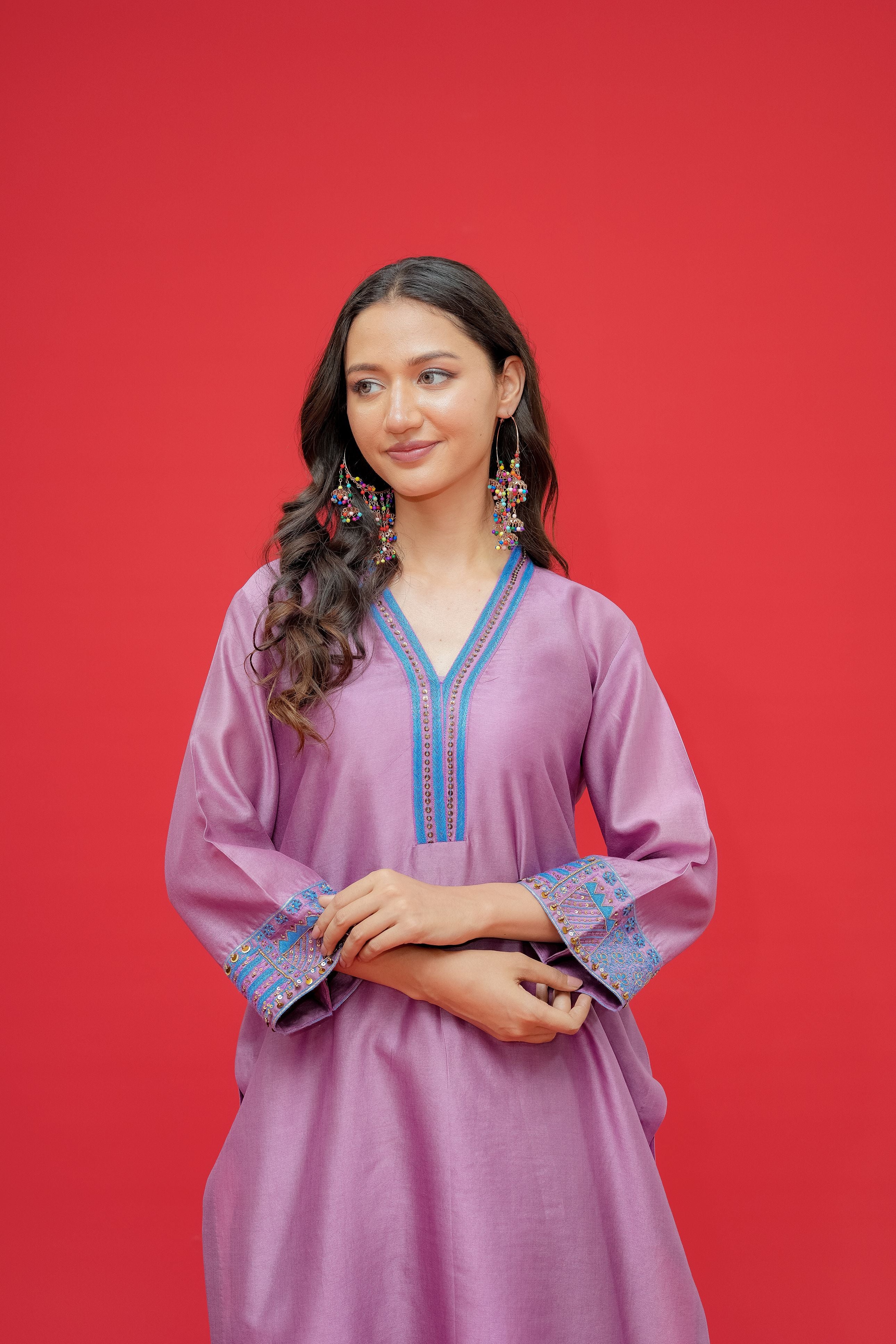 Woman wearing a purple dress with blue embroidery against a red background