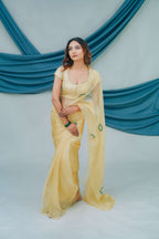 Woman in a yellow saree sitting against a blue draped backdrop