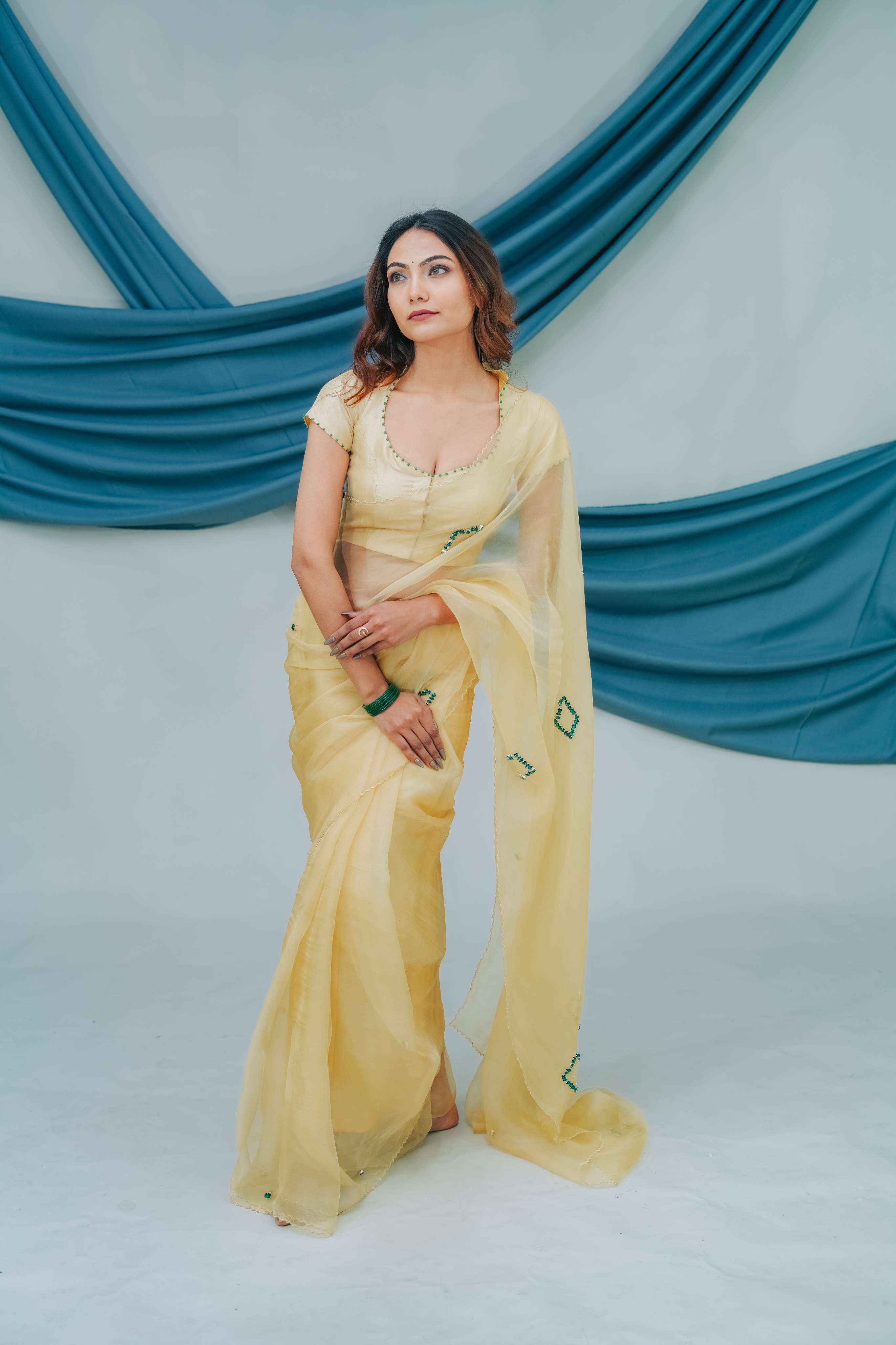 Woman in a yellow saree sitting against a blue draped backdrop