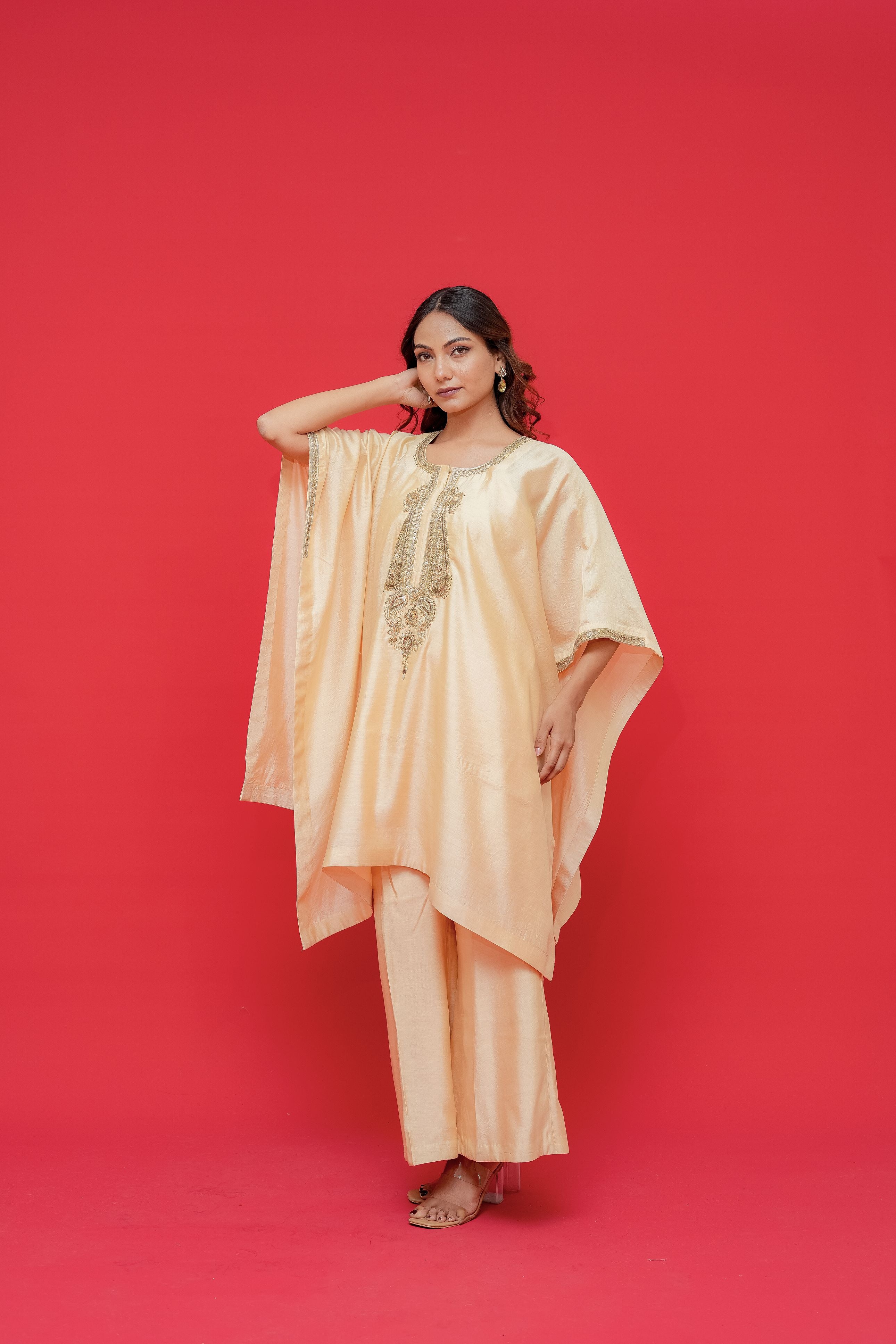 Woman wearing a peach-colored outfit with gold embroidery against a red background