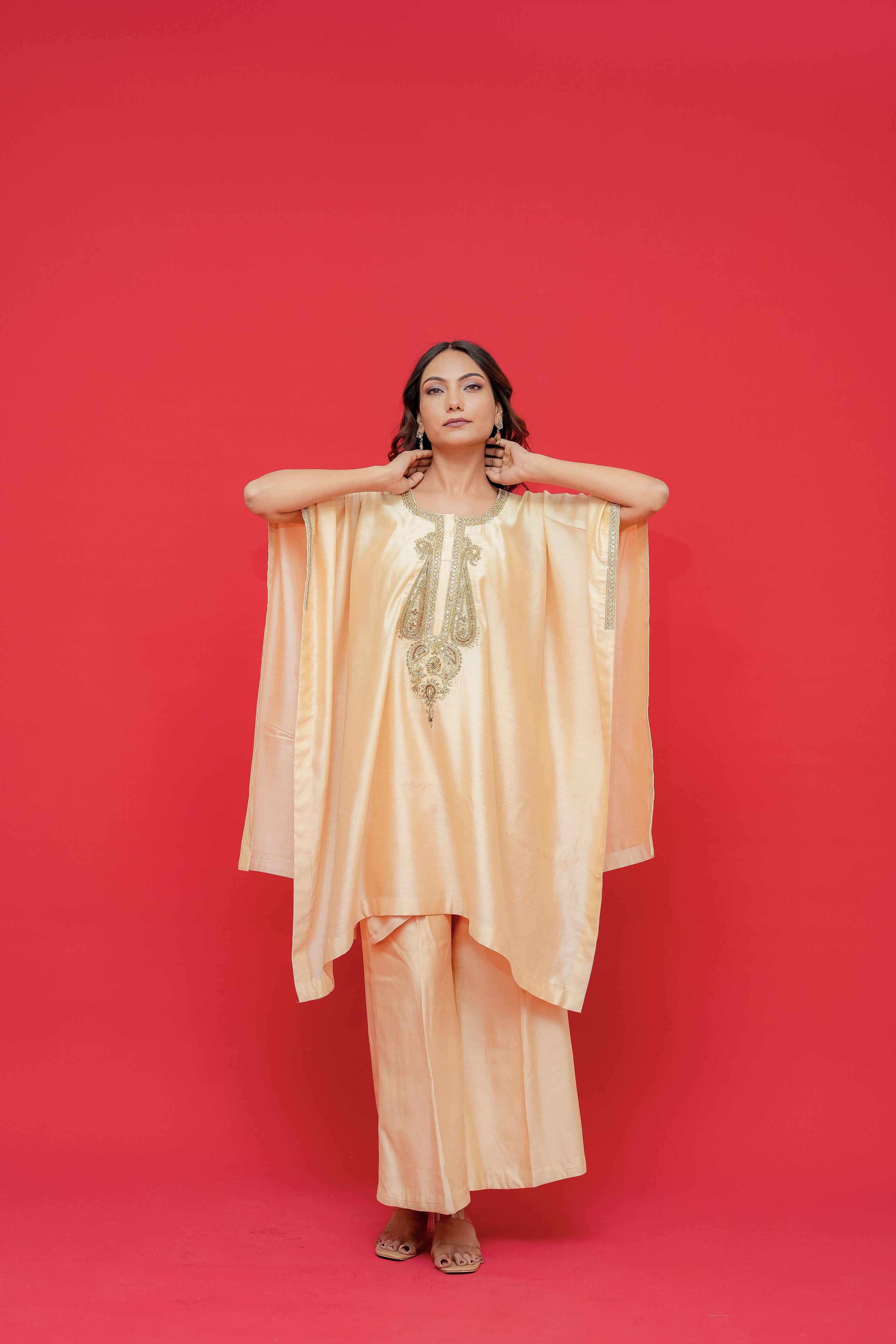 Woman wearing a peach-colored outfit with gold embroidery against a red background