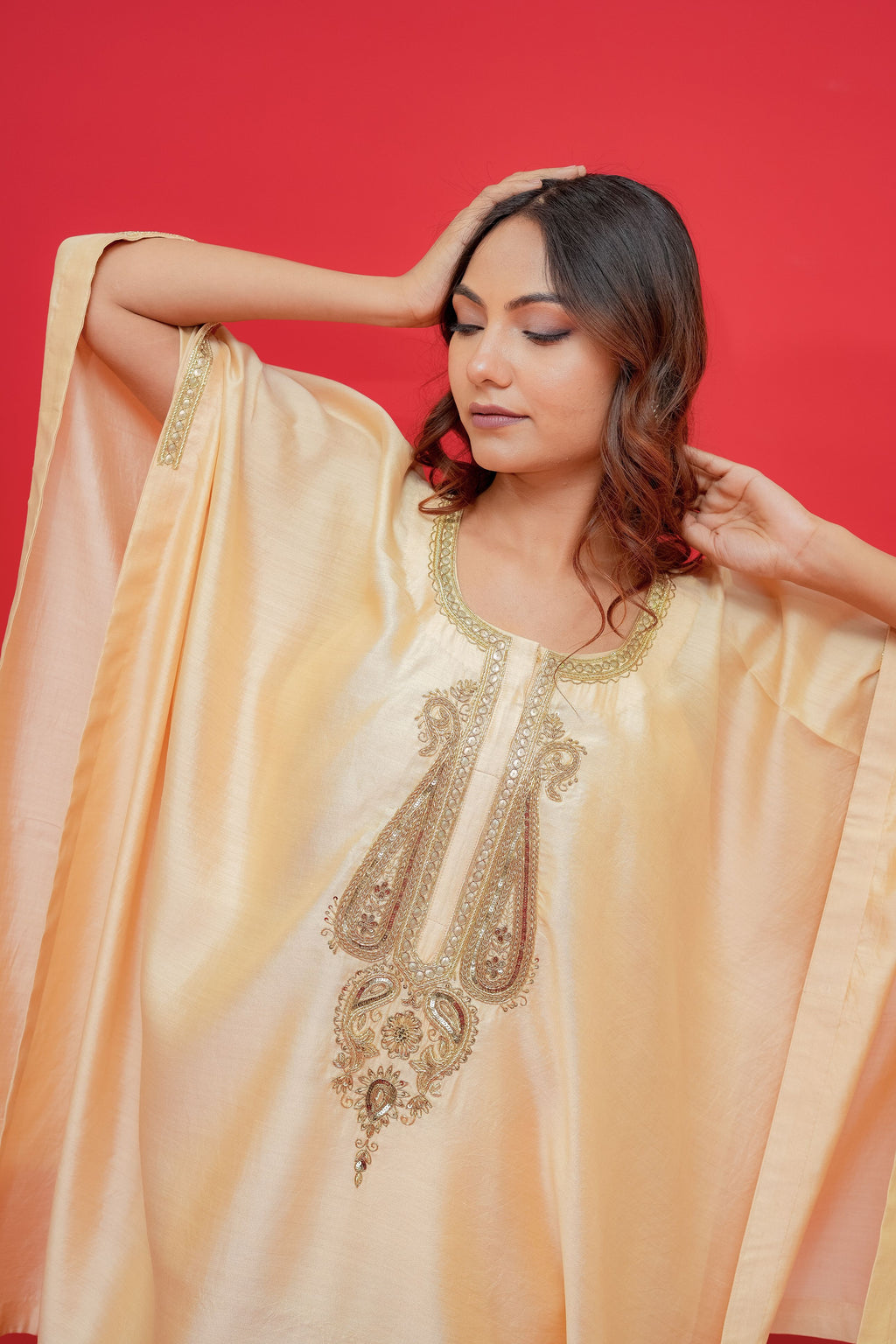 Woman wearing a peach-colored embroidered traditional outfit against a red background