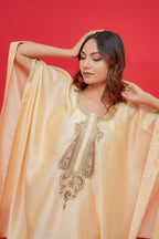 Woman wearing a peach-colored embroidered traditional outfit against a red background