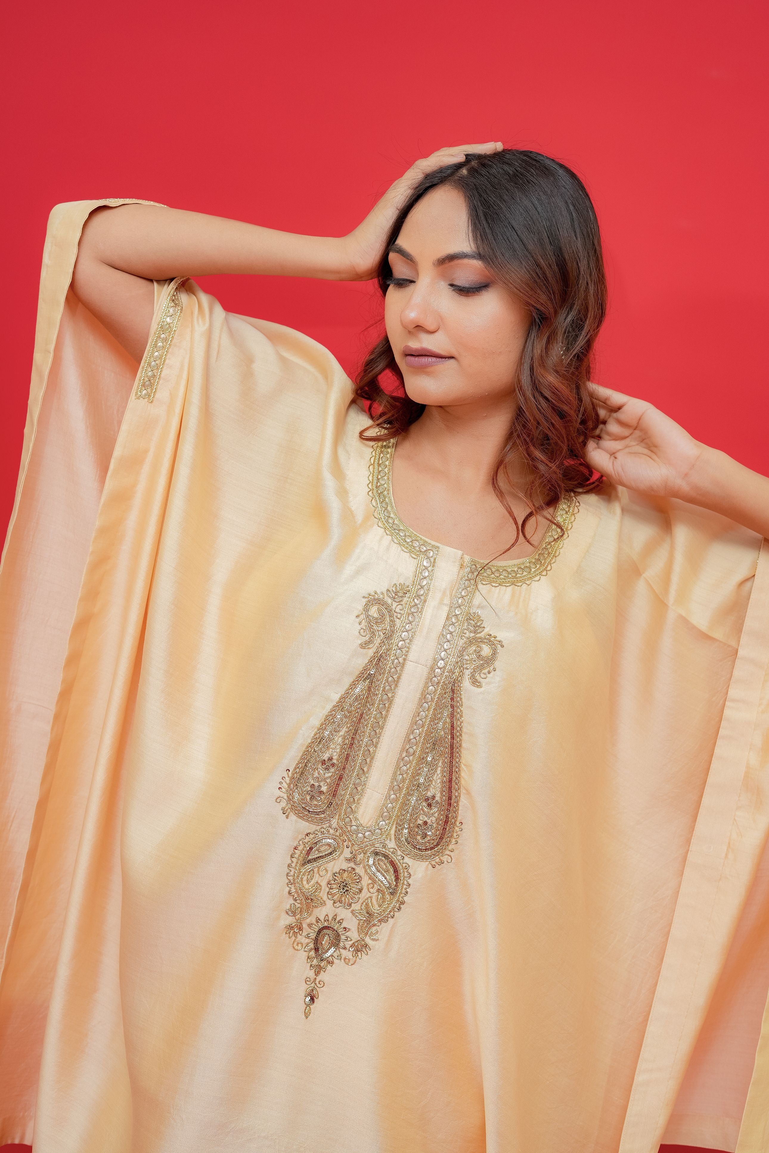 Woman wearing a peach-colored embroidered traditional outfit against a red background