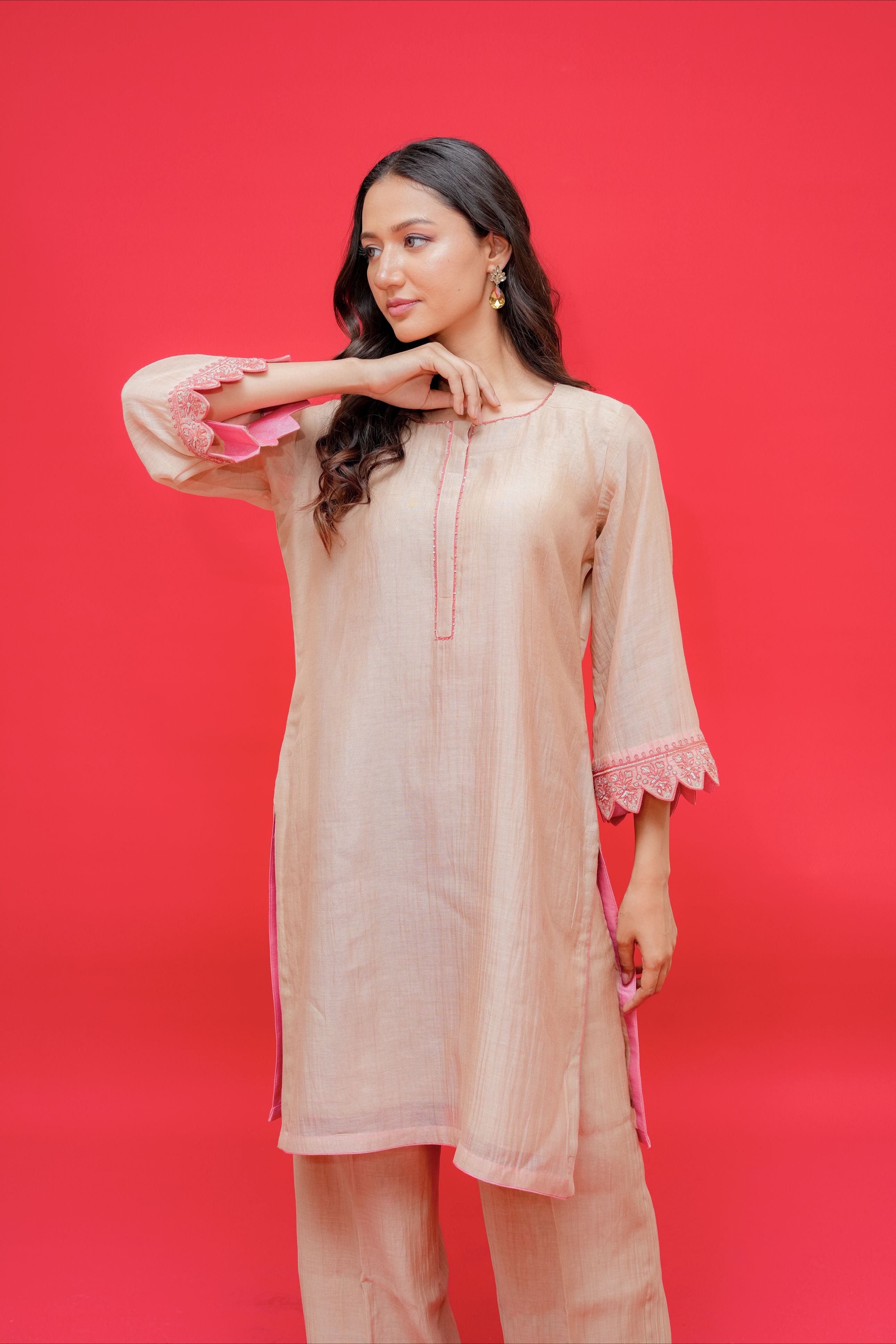 Woman wearing a light pink kurta with lace sleeves against a red background