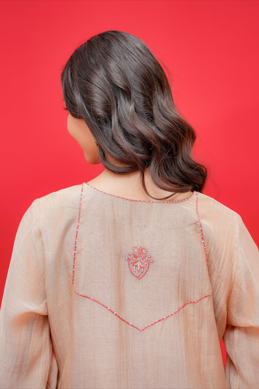 Person wearing a light pink traditional outfit with intricate red embroidery on a red background