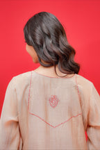 Person wearing a light pink traditional outfit with intricate red embroidery on a red background