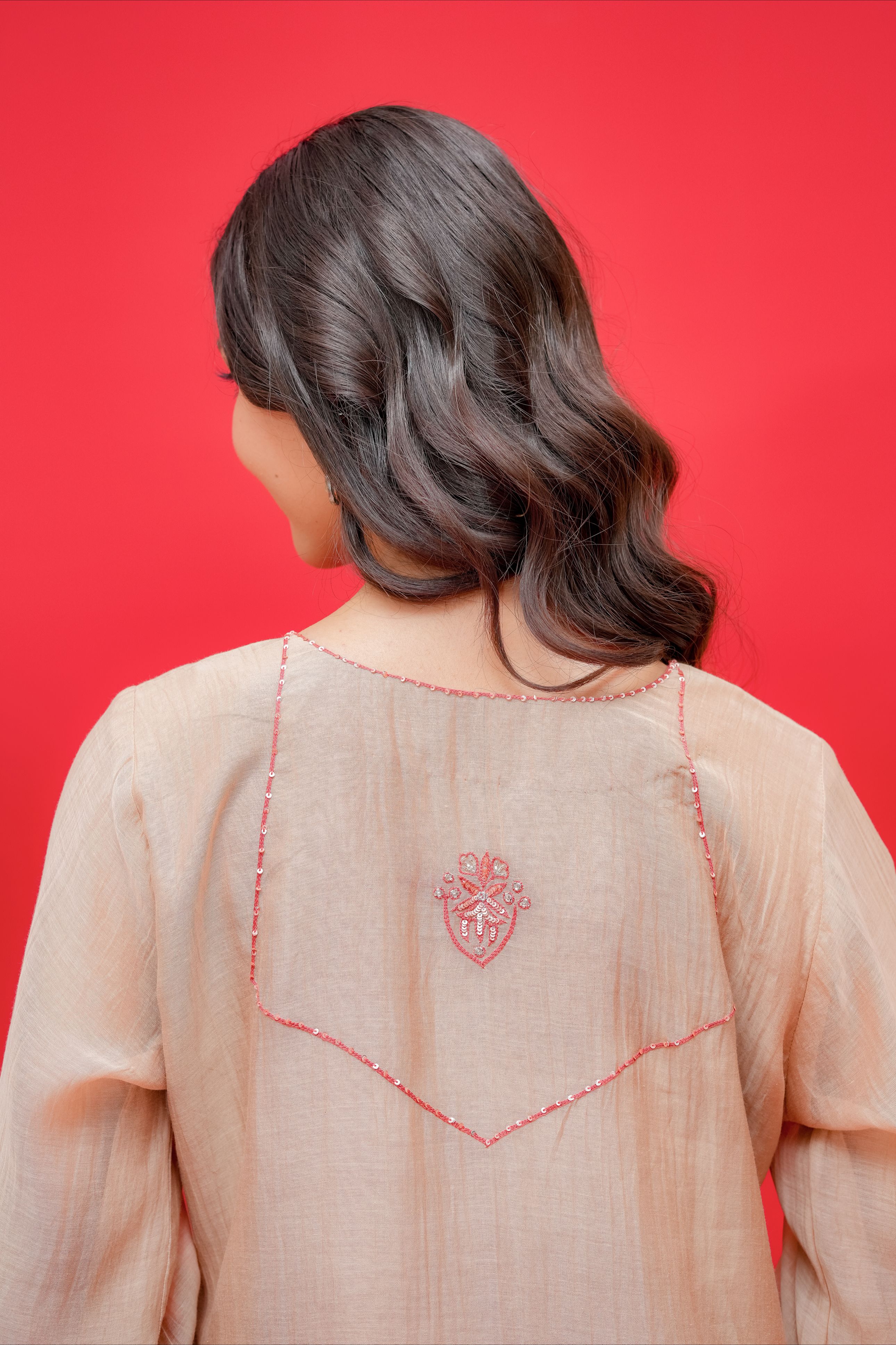 Person wearing a light pink traditional outfit with intricate red embroidery on a red background