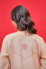 Person wearing a light pink traditional outfit with intricate red embroidery on a red background
