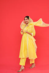 Woman in a yellow traditional outfit with a flowing scarf against a red background
