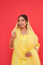 Woman wearing a yellow outfit with a matching dupatta against a red background