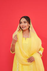 Woman wearing a yellow outfit with a matching dupatta against a red background
