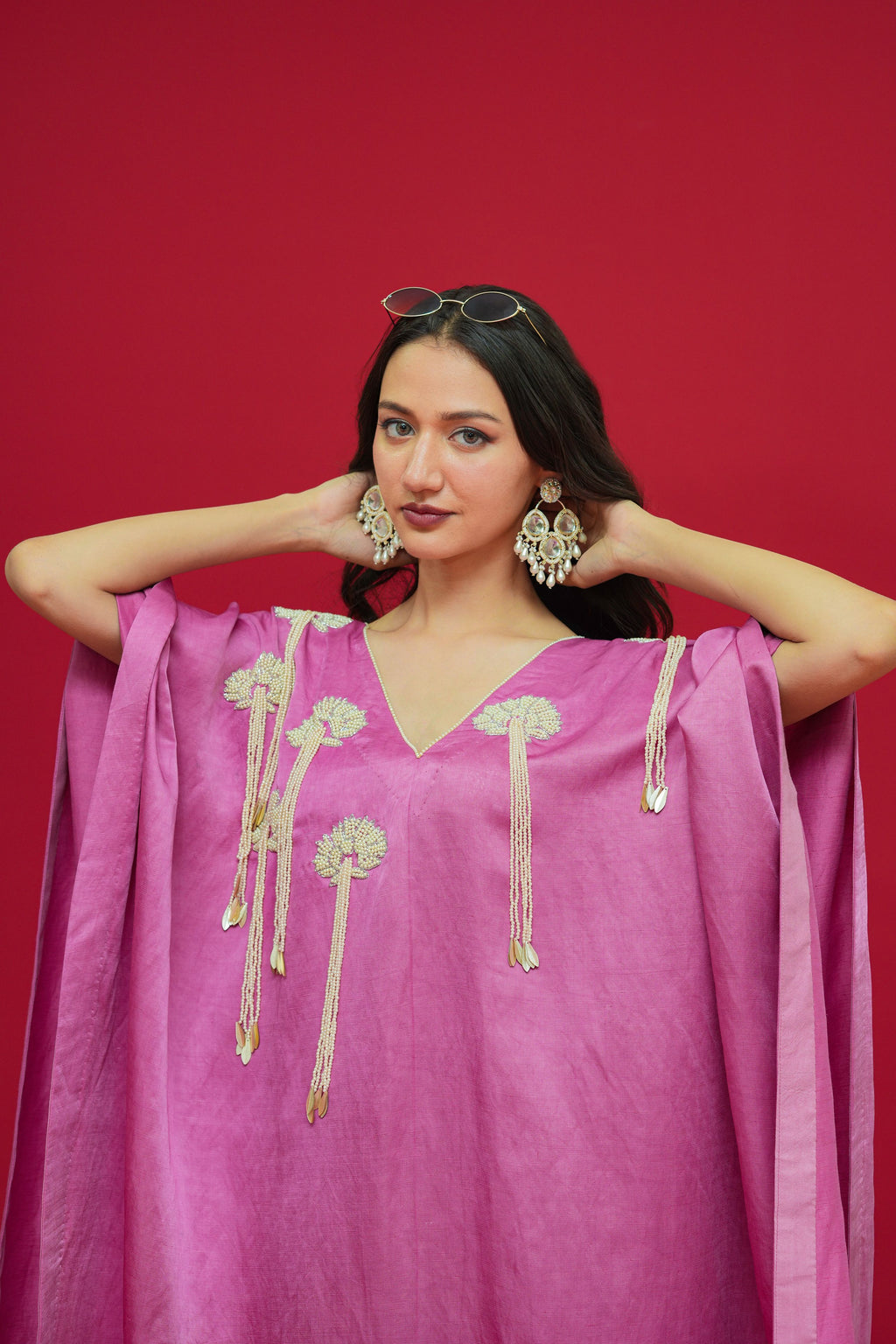 Woman wearing a pink outfit with gold embroidery against a red background