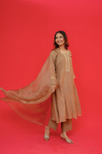 Woman in a beige traditional outfit with a flowing dupatta against a red background