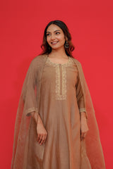 Woman wearing a brown traditional outfit with gold embroidery against a red background