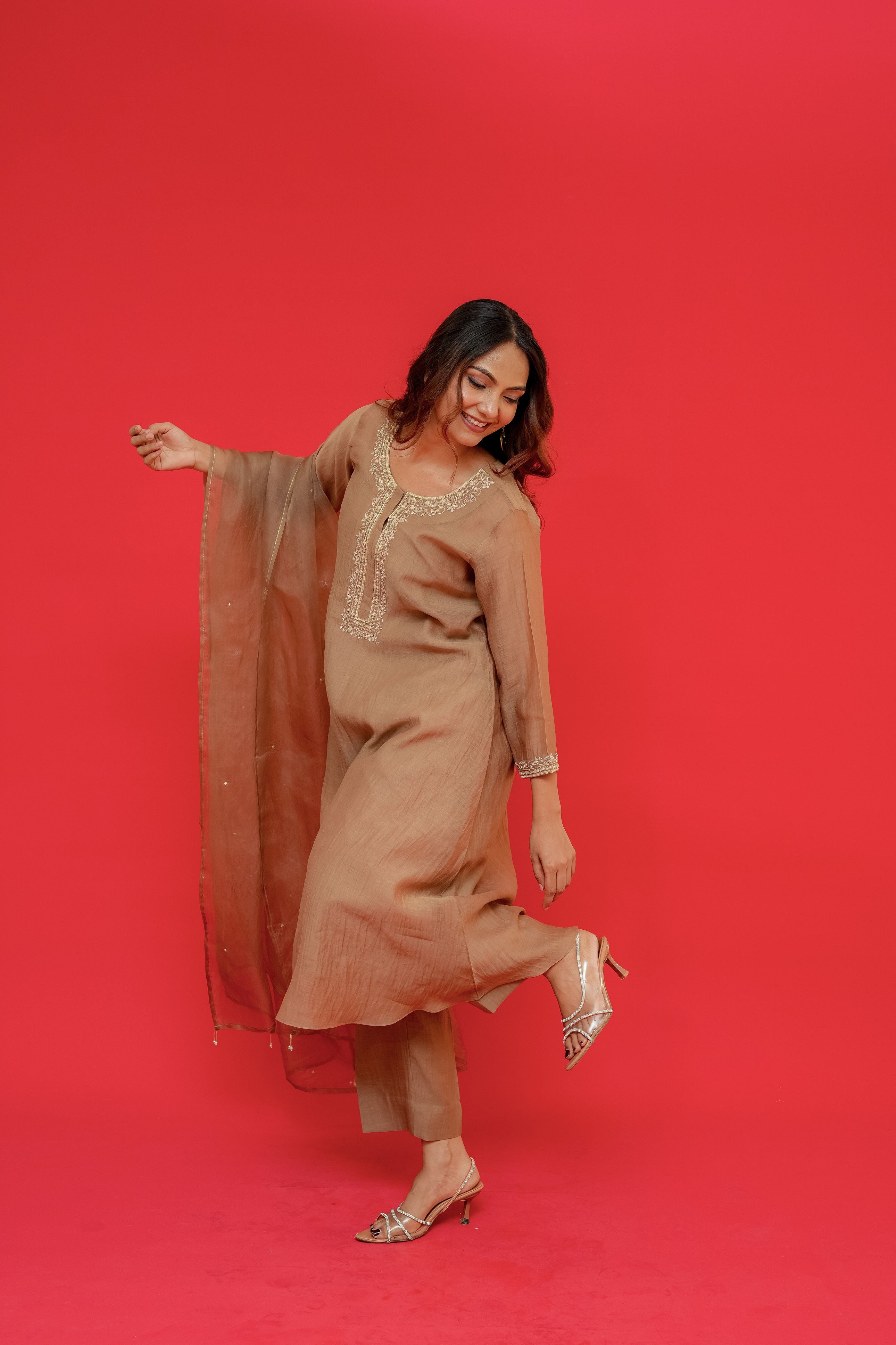 Woman in a beige outfit posing against a red background