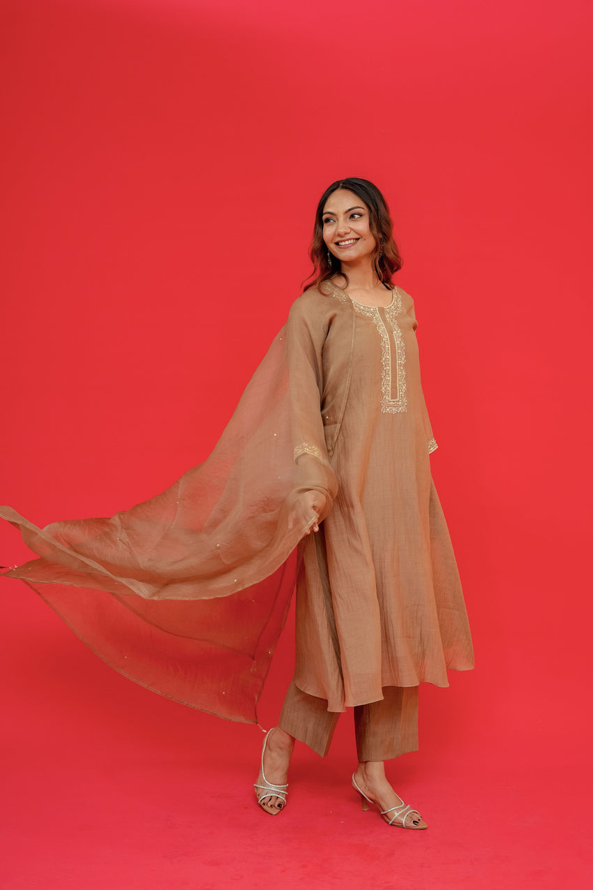Woman in a beige traditional outfit with a flowing dupatta against a red background
