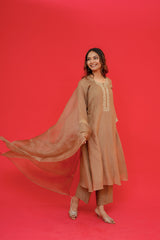 Woman in a beige traditional outfit with a flowing dupatta against a red background