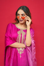 Woman wearing a pink traditional outfit with gold embroidery against a red background