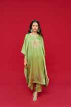 Woman wearing a green traditional outfit with gold embroidery on a red background