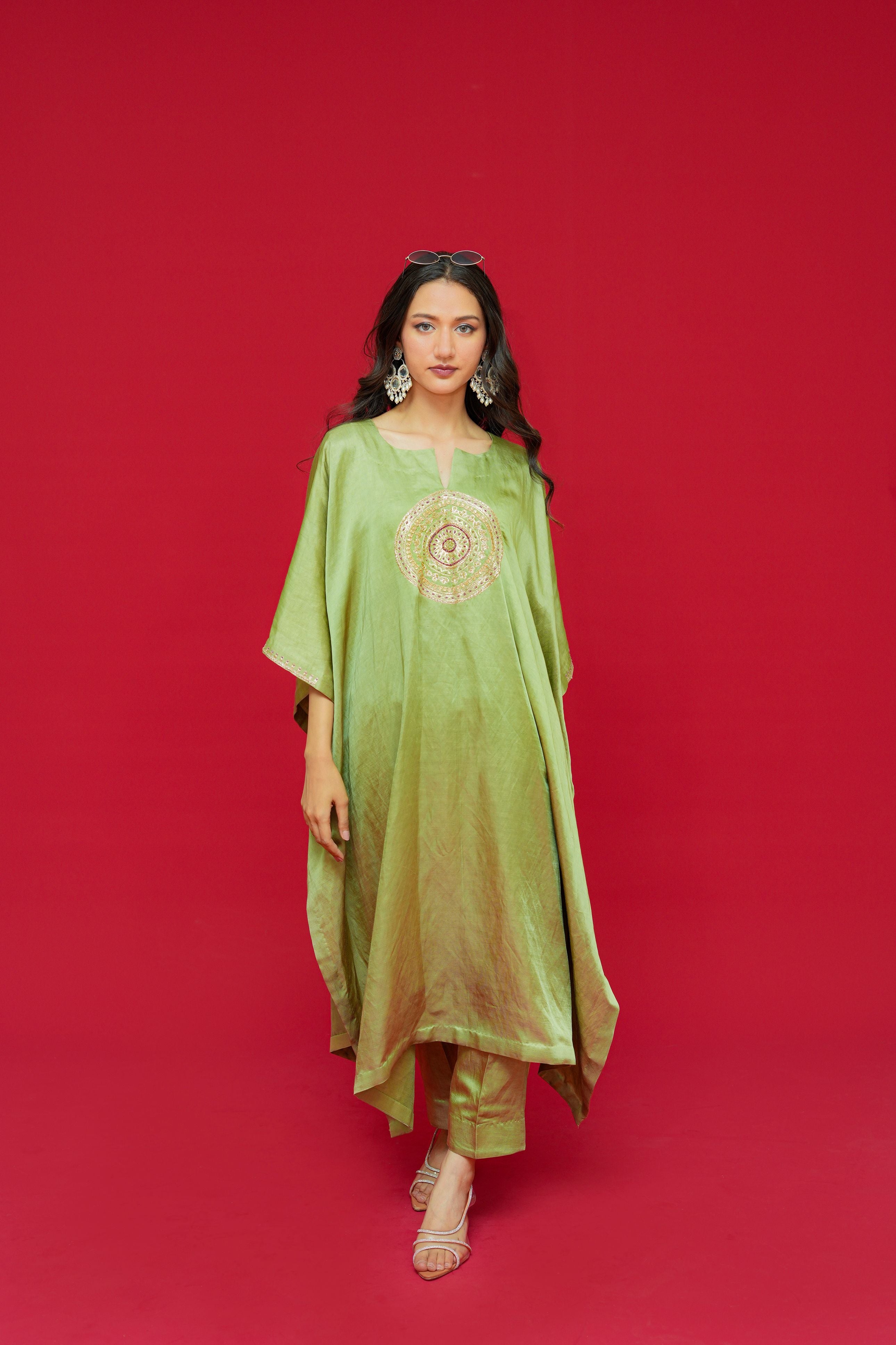 Woman wearing a green traditional outfit with gold embroidery on a red background