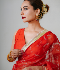 Woman wearing a red saree with gold border against a plain background