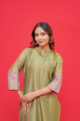 Woman wearing a green kurta with floral embroidery on sleeves against a red background