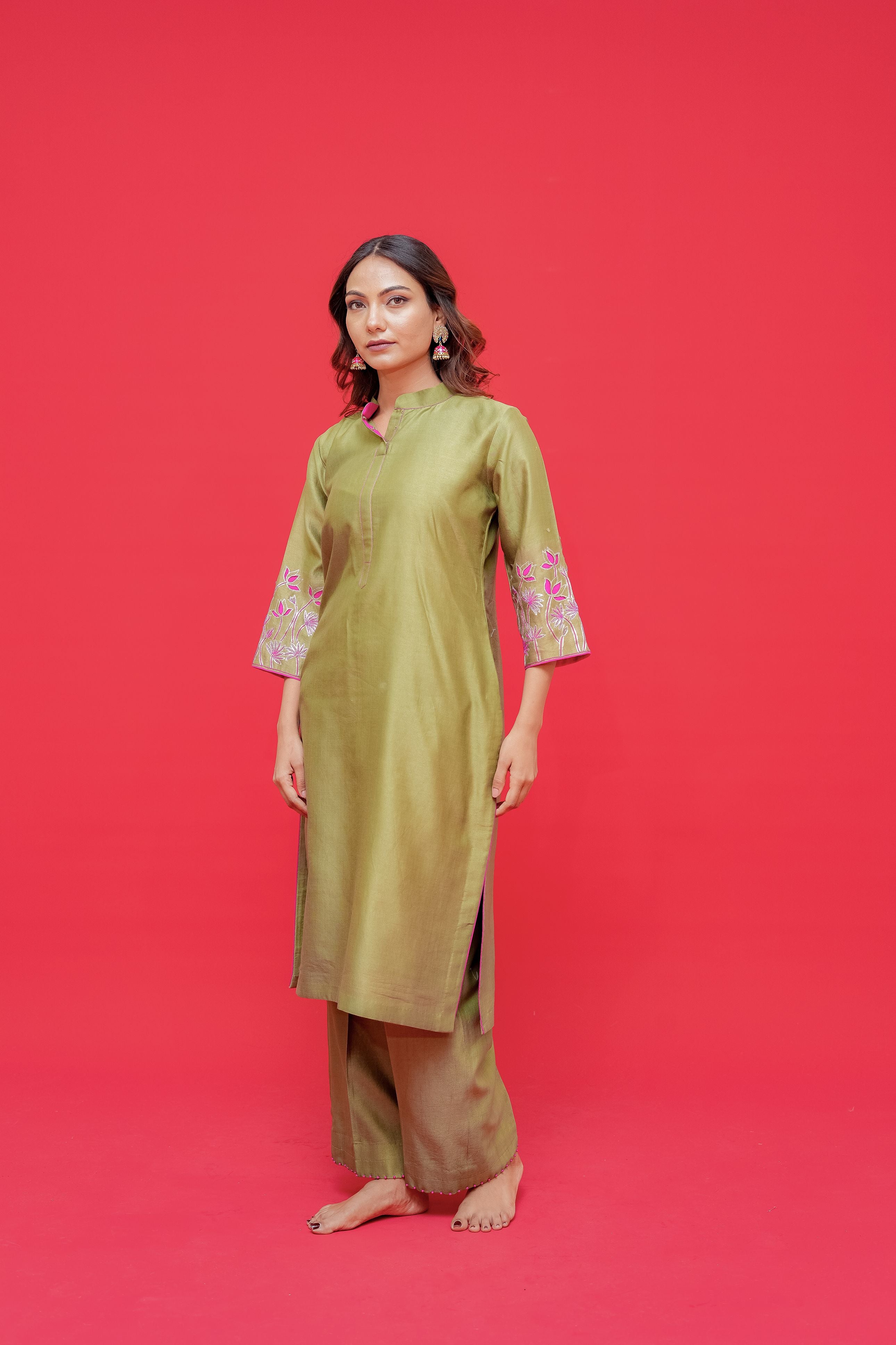 Woman wearing a green traditional outfit with floral embroidery on a red background