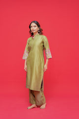 Woman wearing a green traditional outfit with floral embroidery on a red background