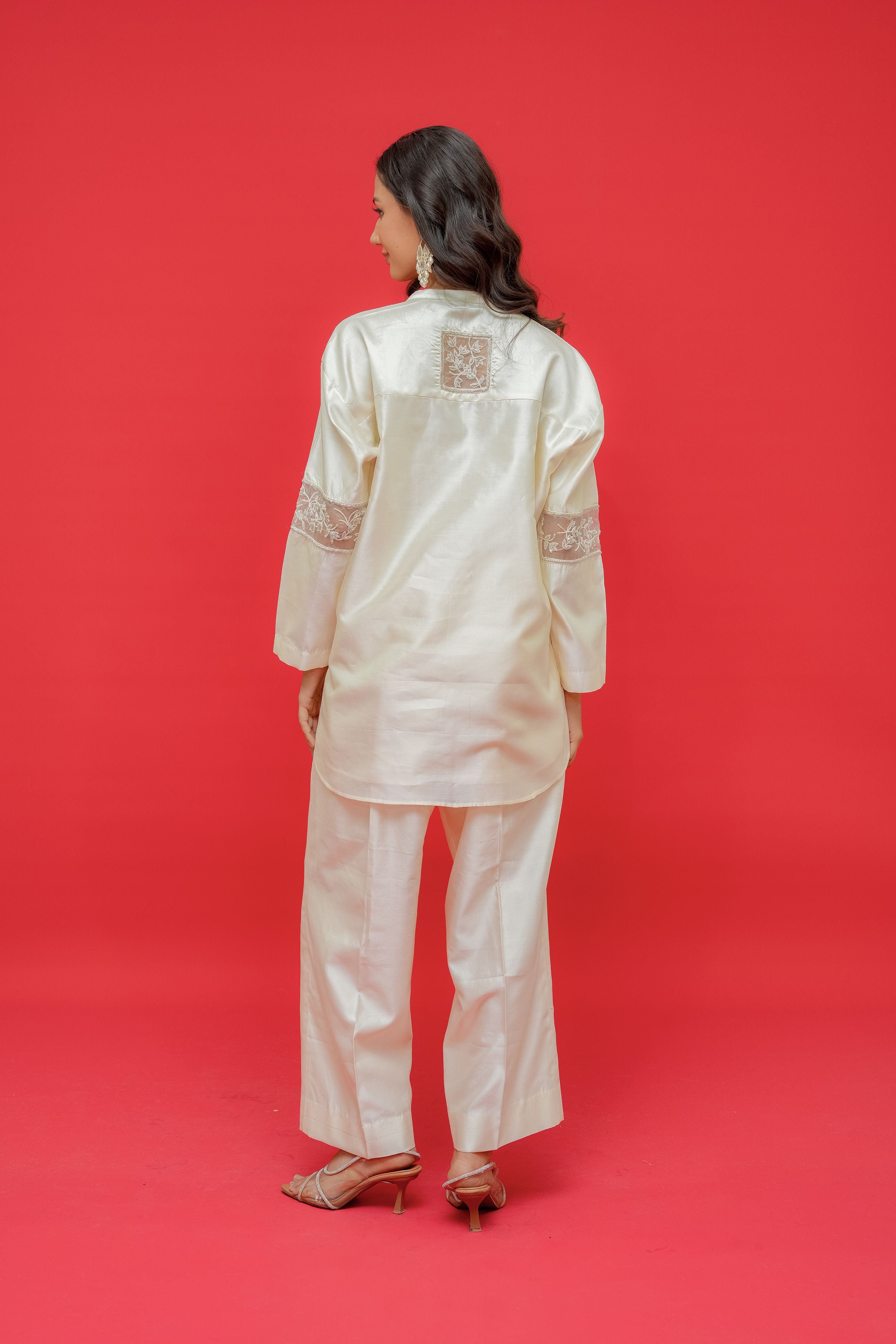 Woman wearing a cream-colored traditional outfit with intricate designs on a red background