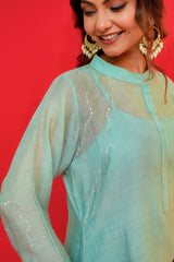 Woman wearing a light blue sheer top with sequin details against a red background