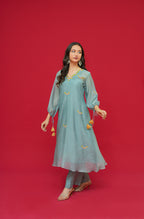 Woman wearing a light blue traditional outfit with gold details on a red background
