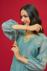 Woman wearing a light blue embroidered dress against a red background