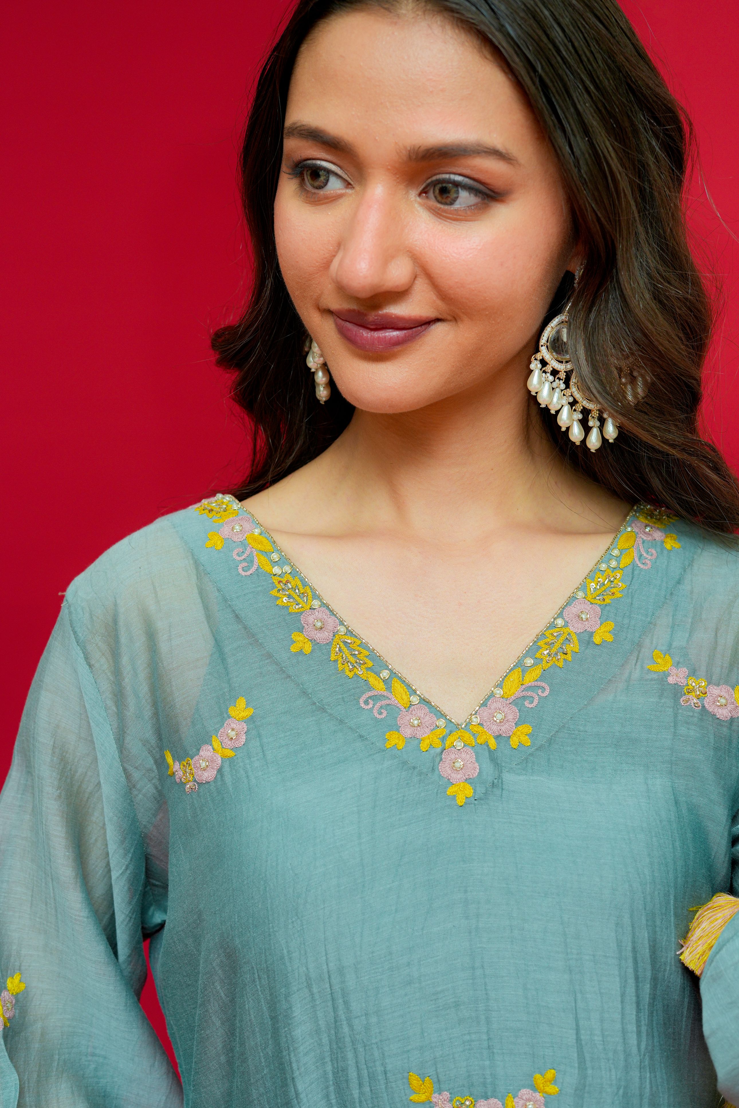 Woman wearing a teal embroidered dress against a red background