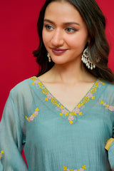 Woman wearing a teal embroidered dress against a red background