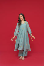 Woman wearing a teal traditional outfit with gold embroidery on a red background