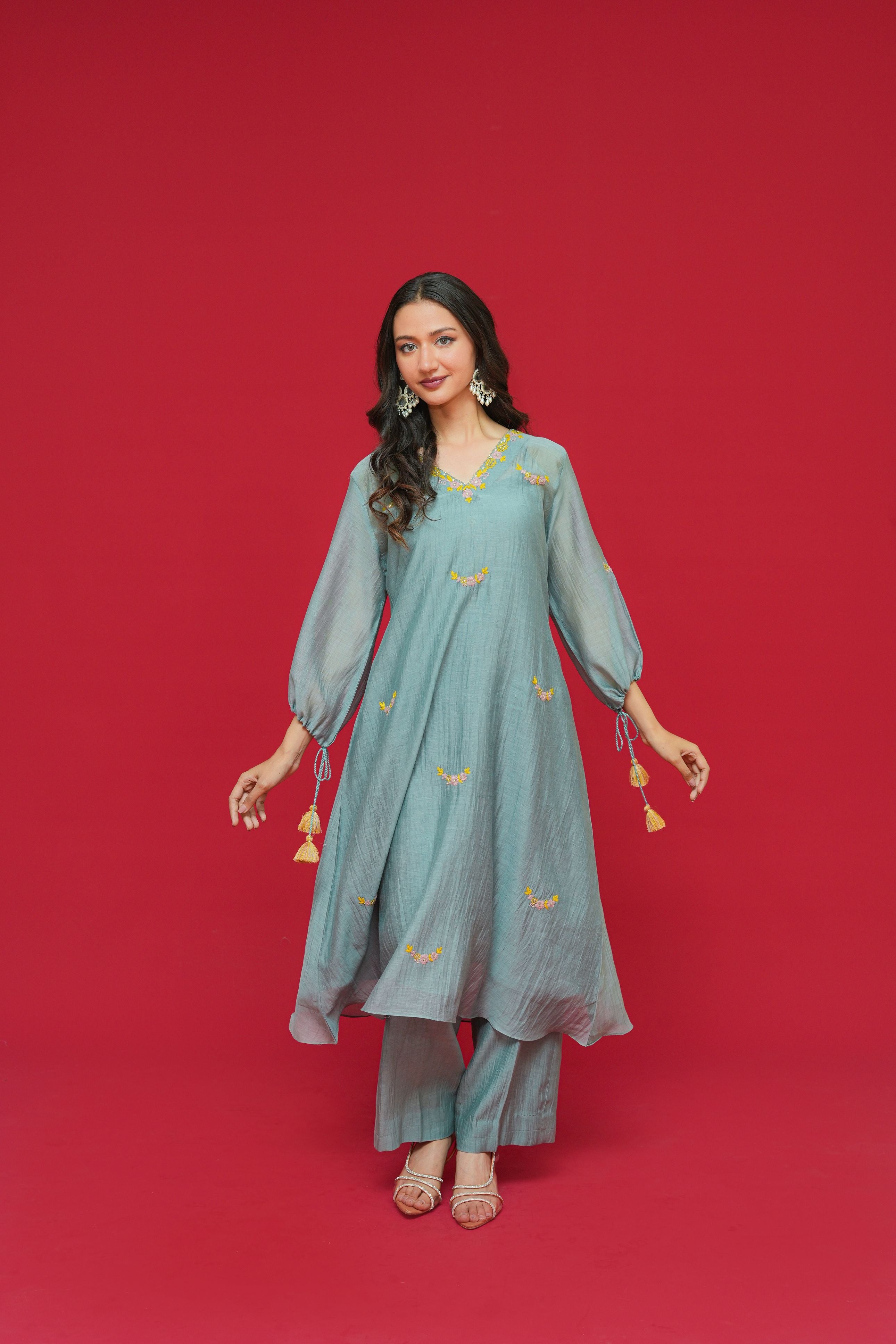 Woman wearing a teal traditional outfit with gold embroidery on a red background