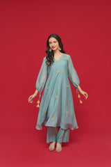 Woman wearing a teal traditional outfit with gold embroidery on a red background