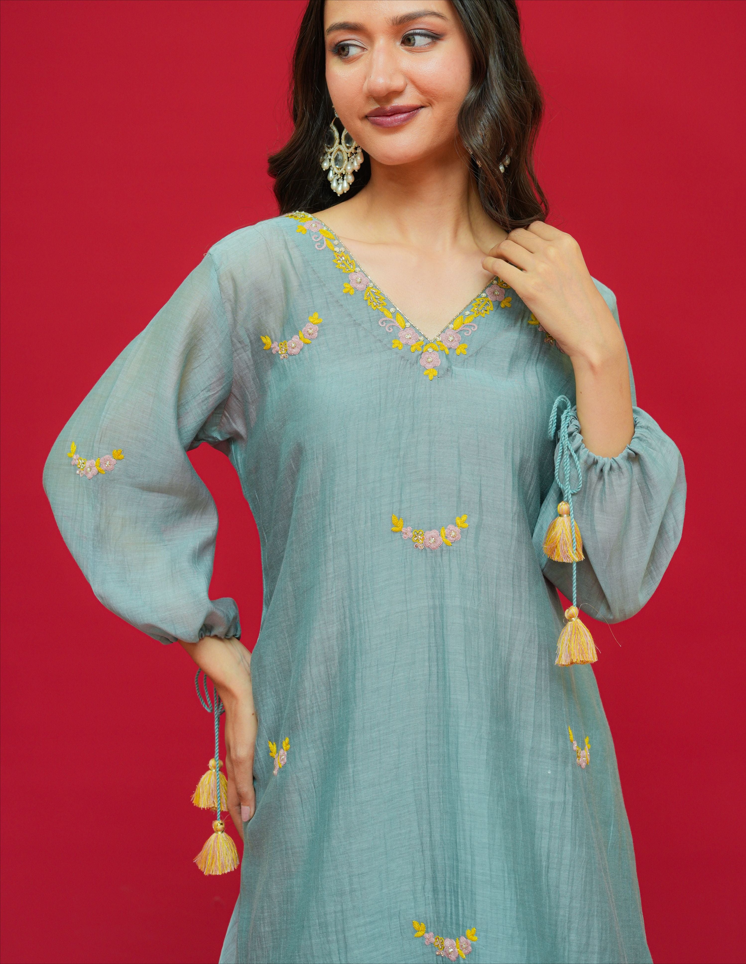 Woman wearing a light blue embroidered dress with yellow details on a red background
