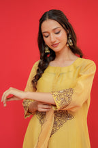 Woman wearing a yellow traditional outfit with intricate designs on a red background