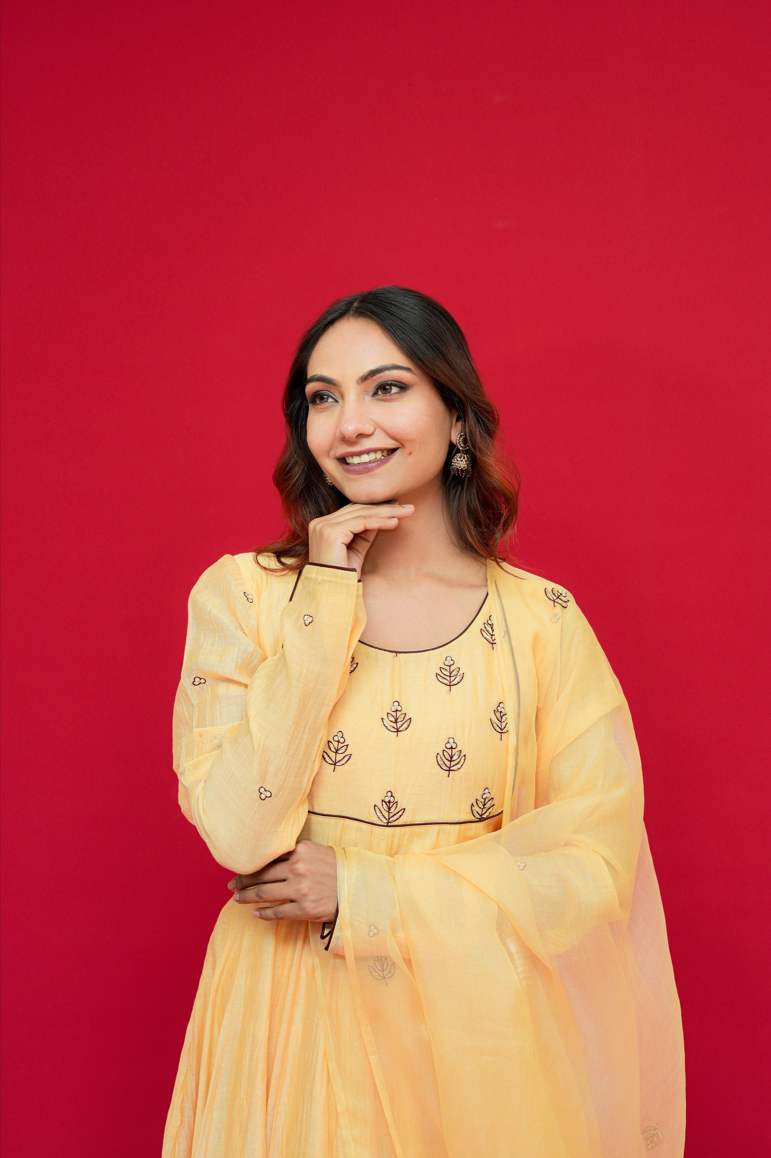 Woman wearing a Sunny Yellow Mul Chanderi Anarkali Set  against a red background
