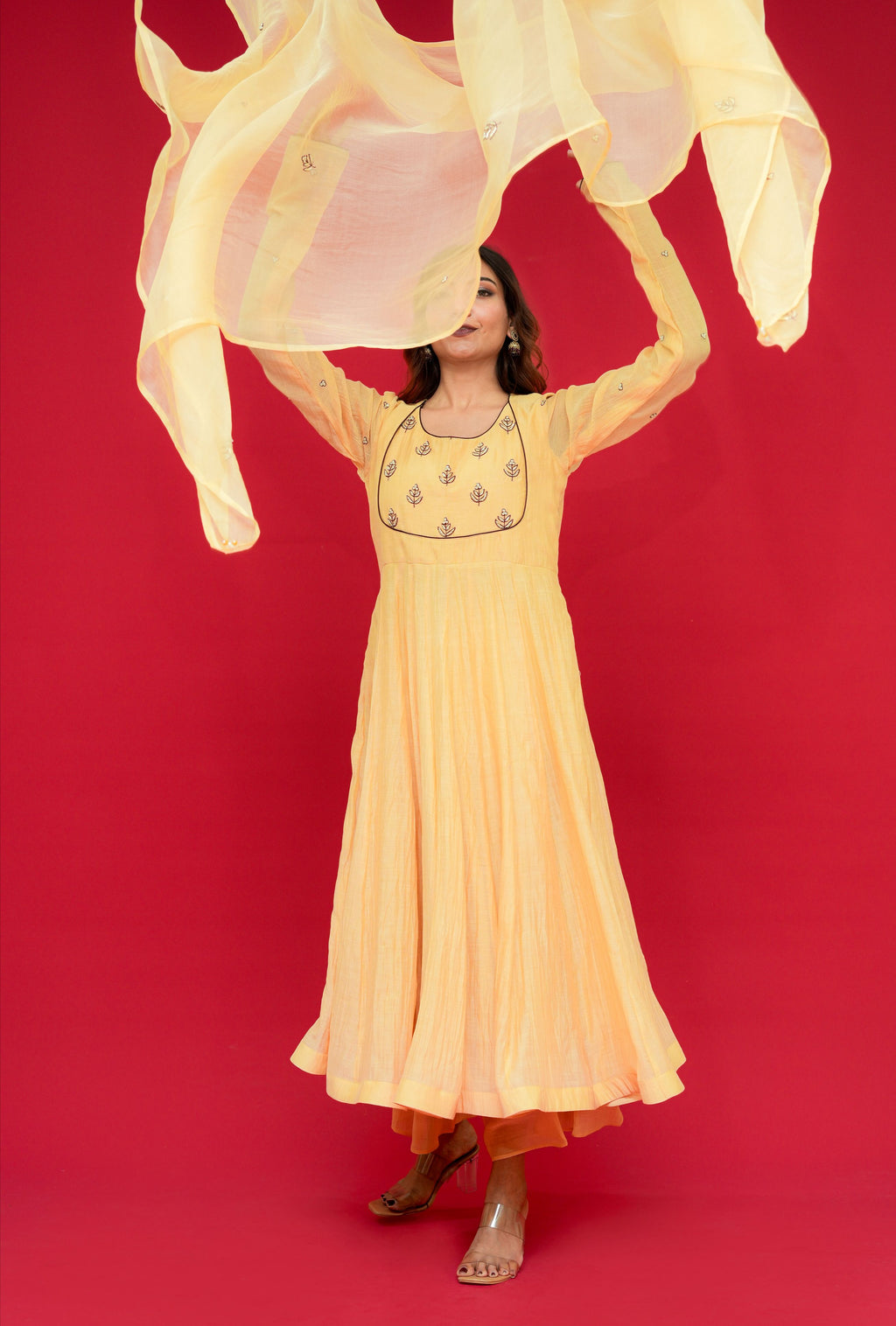 Woman in a long Sunny Yellow Mul Chanderi Anarkali Set  against a red background