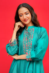 Woman wearing a teal embroidered dress against a red background