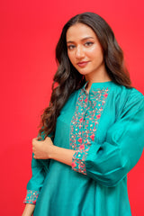 Woman wearing a teal traditional outfit with floral embroidery on a red background