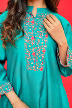 Teal embroidered dress with floral patterns on a red background